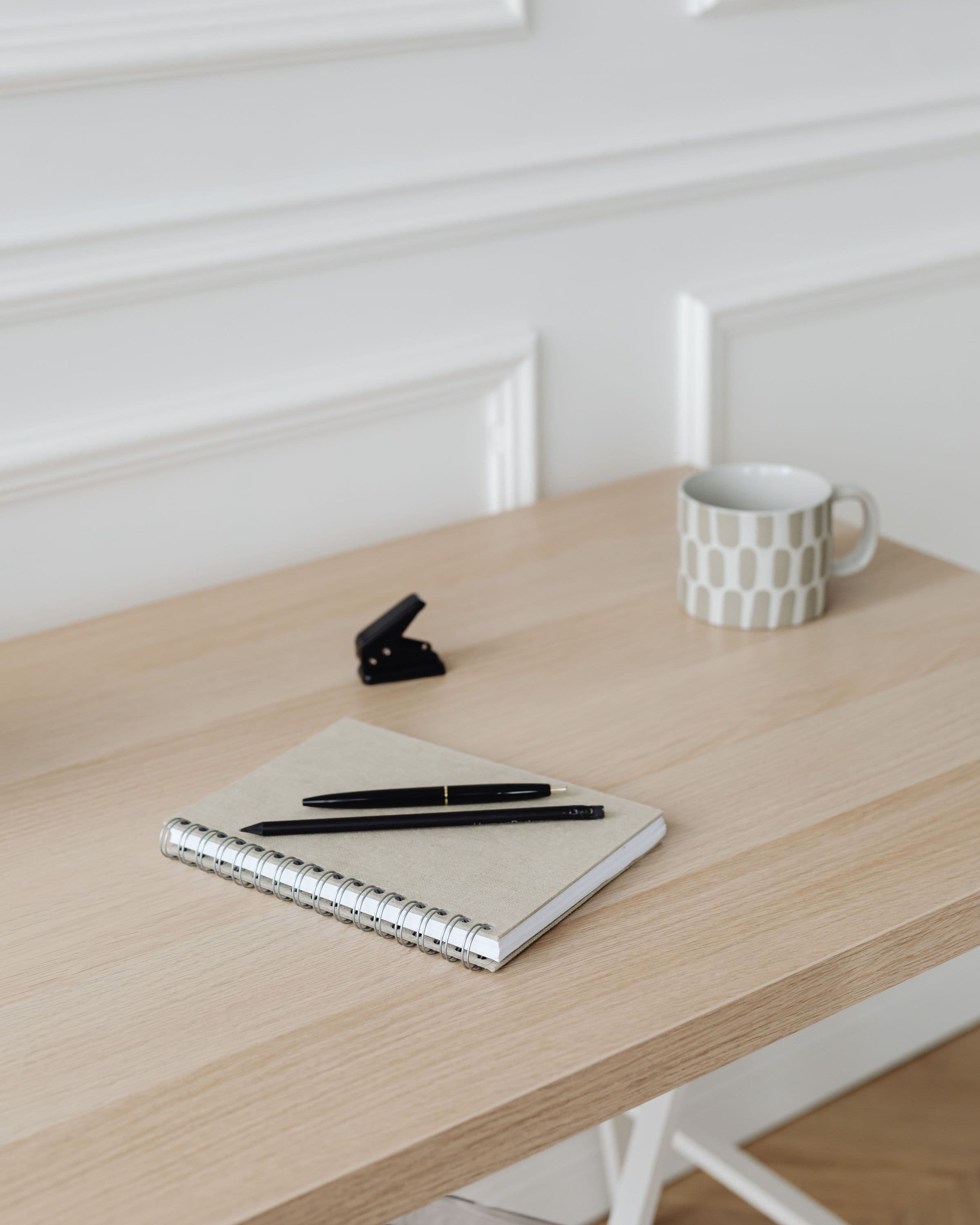 Notizbuch mit Stift und Kaffeetasse auf einem hellen Holztisch