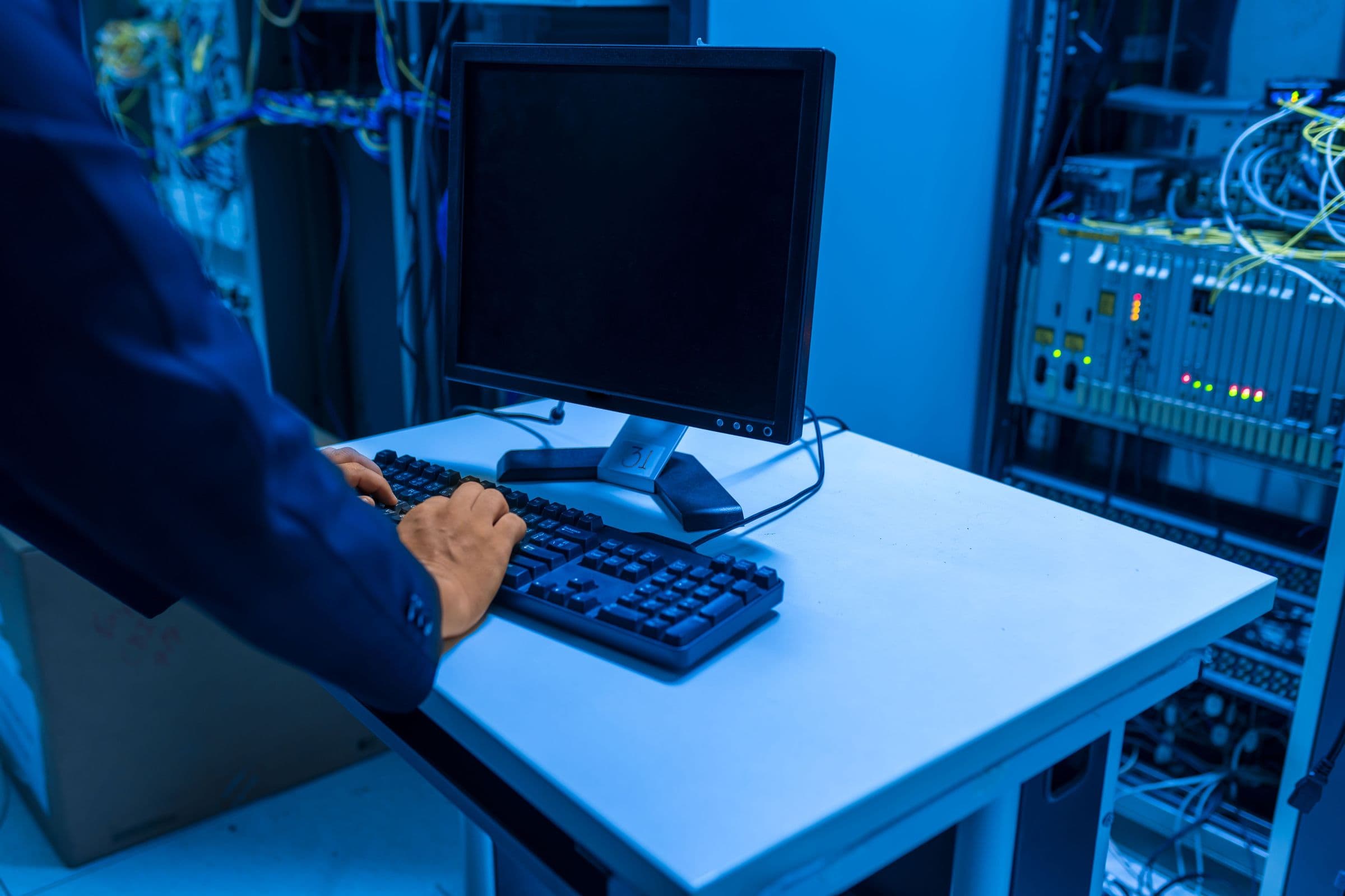 Administrator an der Tastatur vor einem Serverschrank mit blinkenden Netzwerkkomponenten